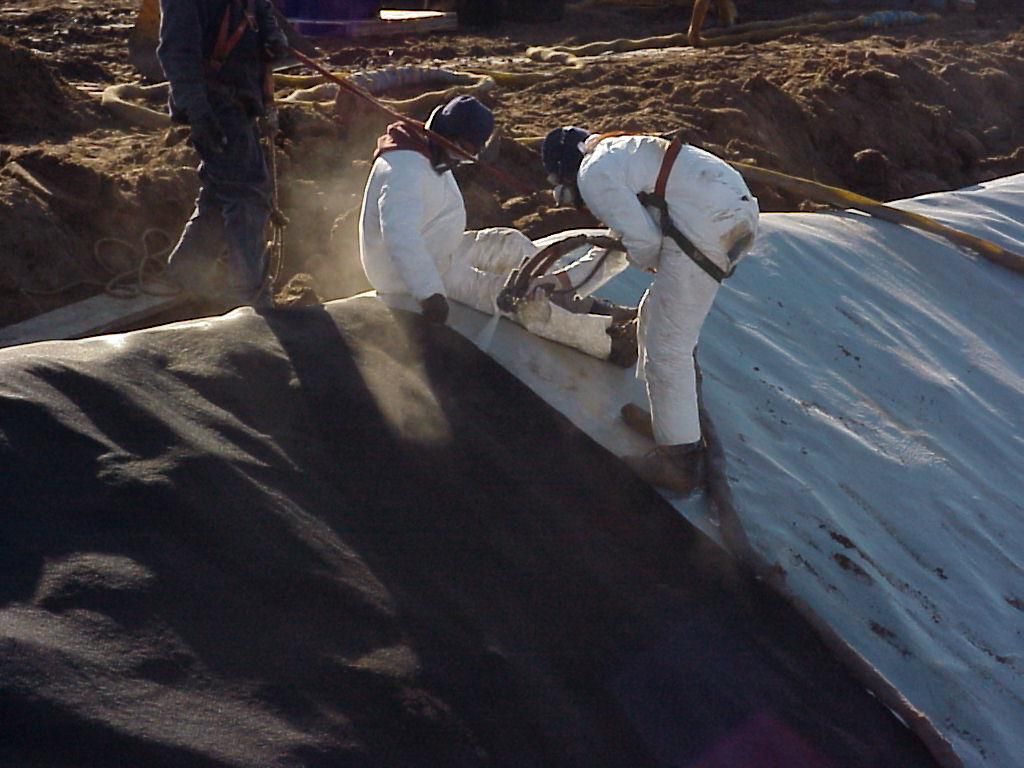 Workers in white suits spreading dark material over a large plastic-covered surface