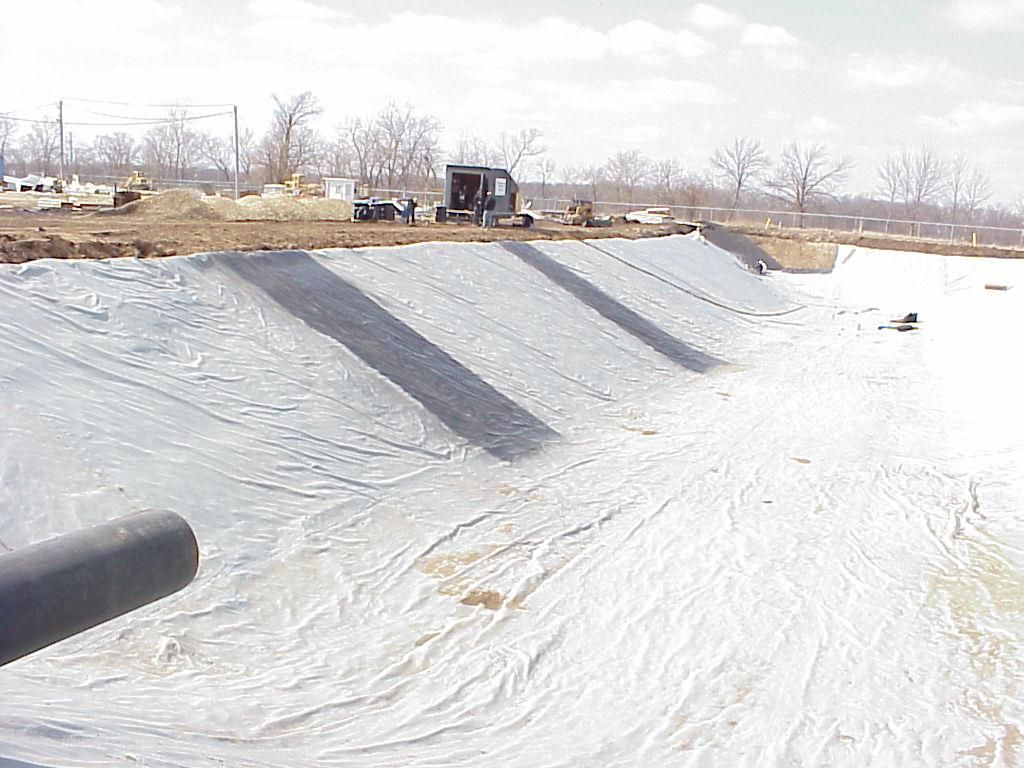 Snow-covered empty drainage ditch with a small excavator in the background