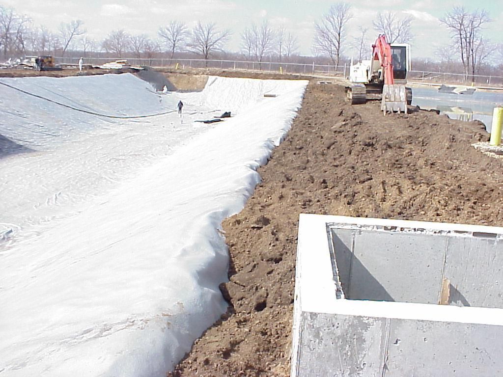Excavator working beside a snow-covered canal in a muddy construction area