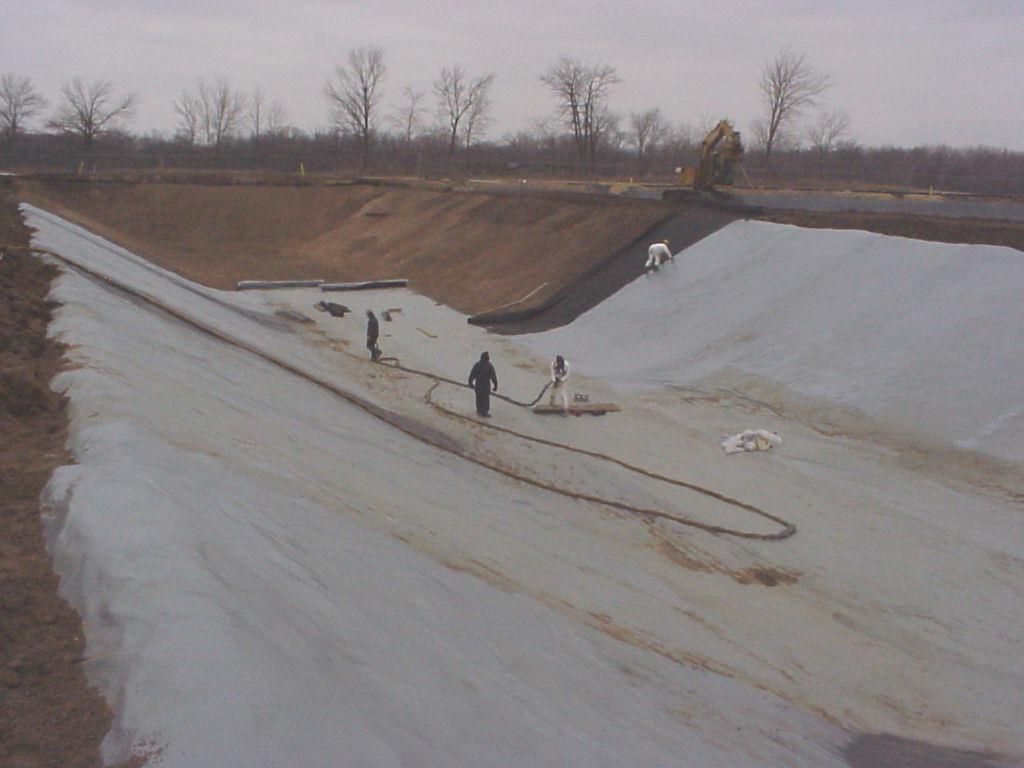 Workers lining a concrete drainage canal under construction, with heavy equipment on the slope.