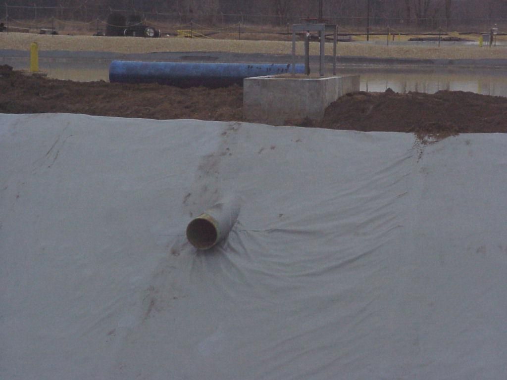Large drainage pipe opening in a white-lined ditch or pond near a construction site