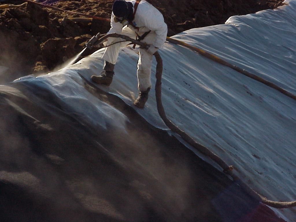 Worker using a hose on a rooftop, spraying water across dark sloped shingles