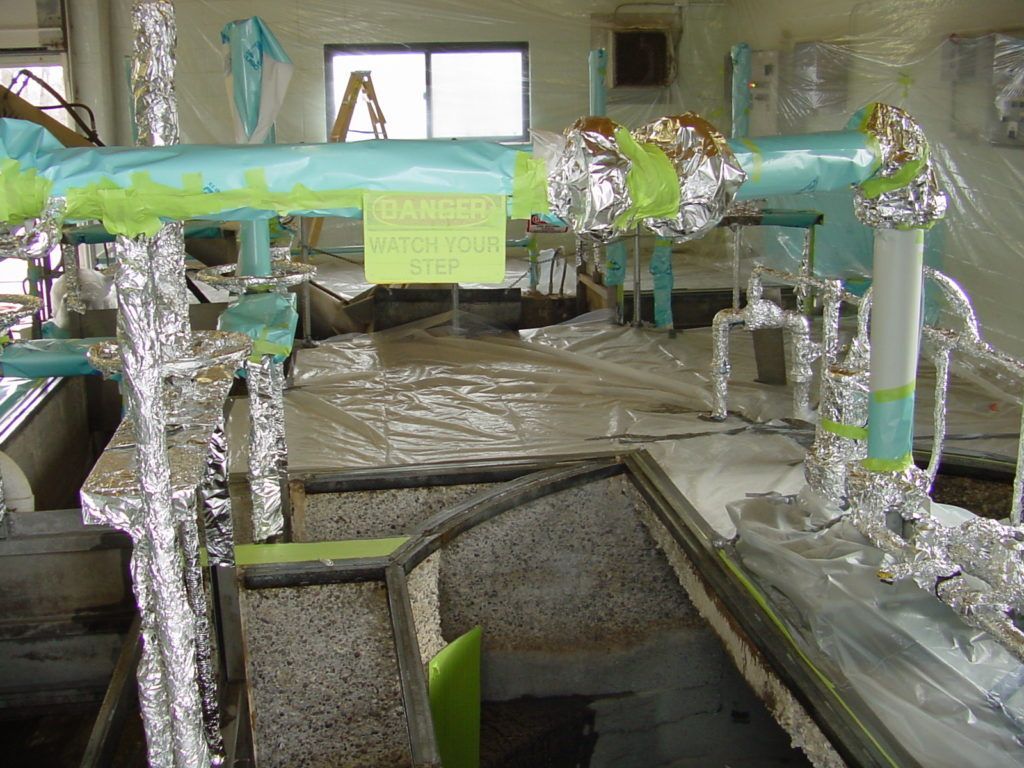 Foil-covered indoor setup with pipes and a yellow warning sign in a room with windows