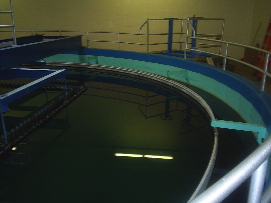 Curved conveyor belt in a dim industrial facility, with blue railings and metal platforms.