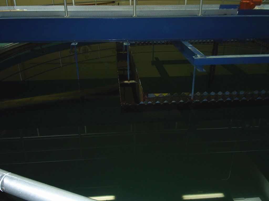 Dim industrial interior with blue beams, dark machinery, and fluorescent lights reflecting below.