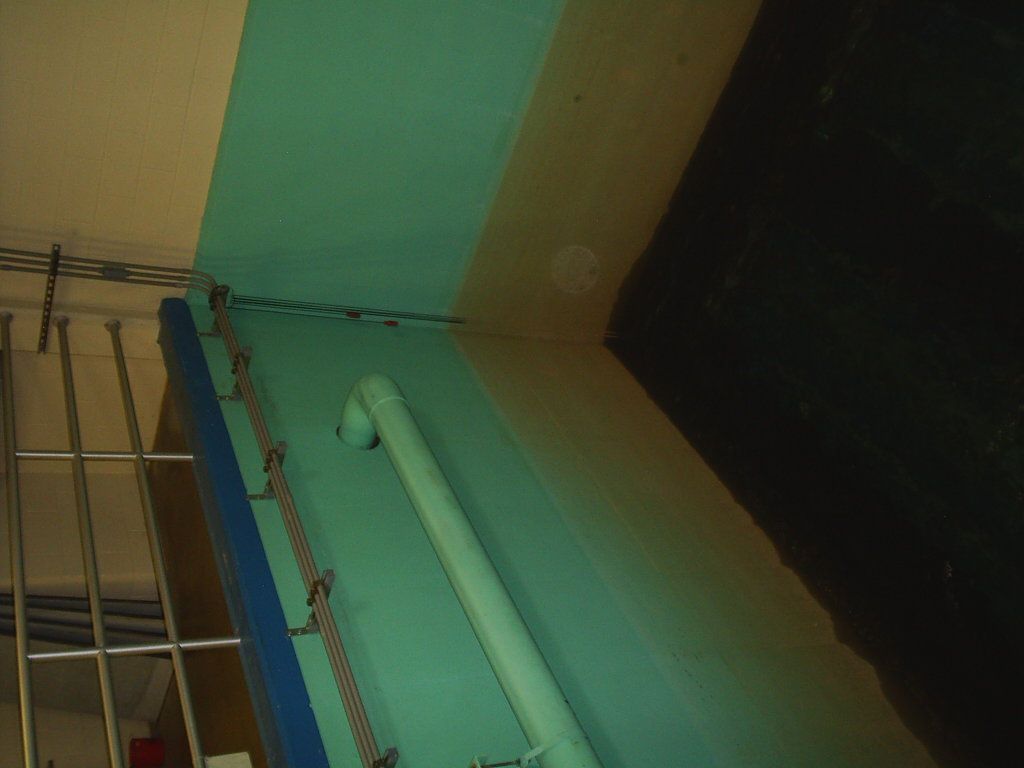 Indoor corner with turquoise wall, exposed pipes, and a metal rail against the ceiling.