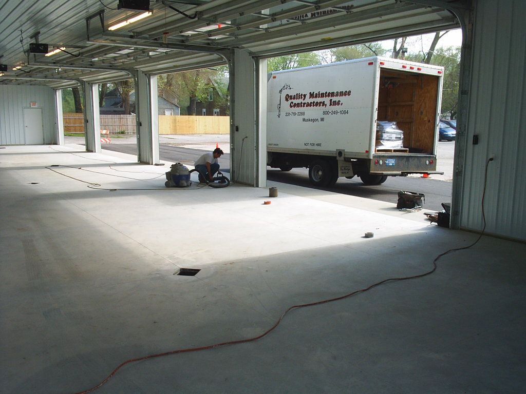 Open warehouse with a truck parked inside, a person near tools, and cables across the concrete floor.