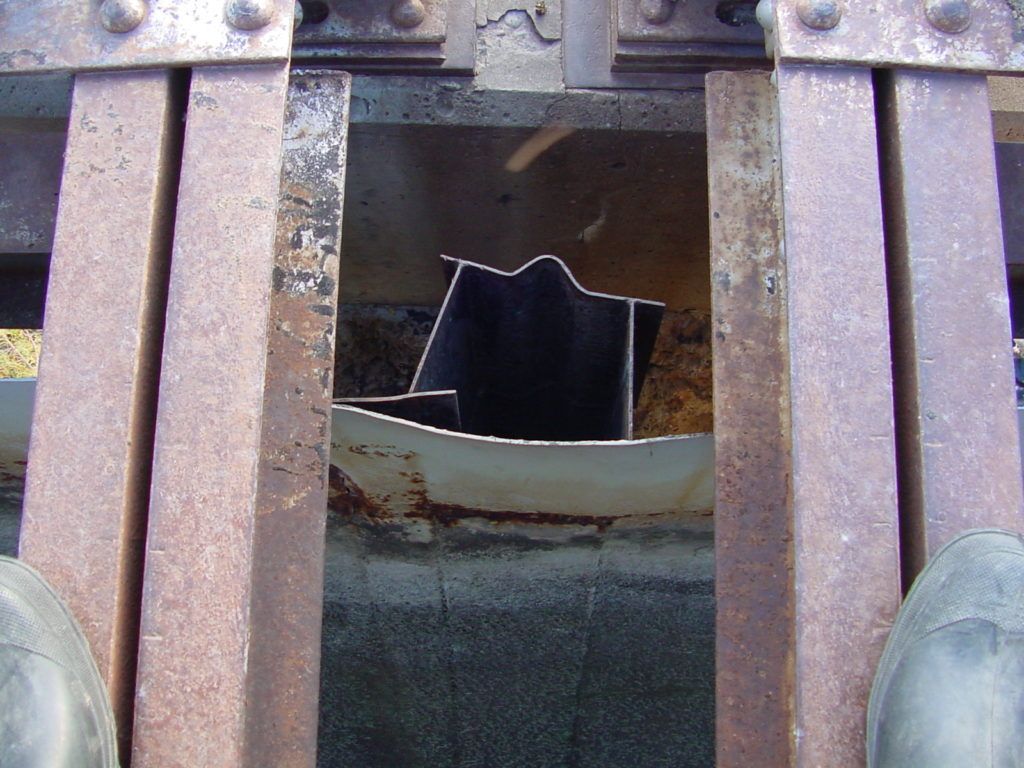 Broken black object wedged between rusty metal bars over a dirty drain opening