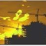 Silhouette of a person on a rooftop at sunset with a yellow-orange sky and construction cranes