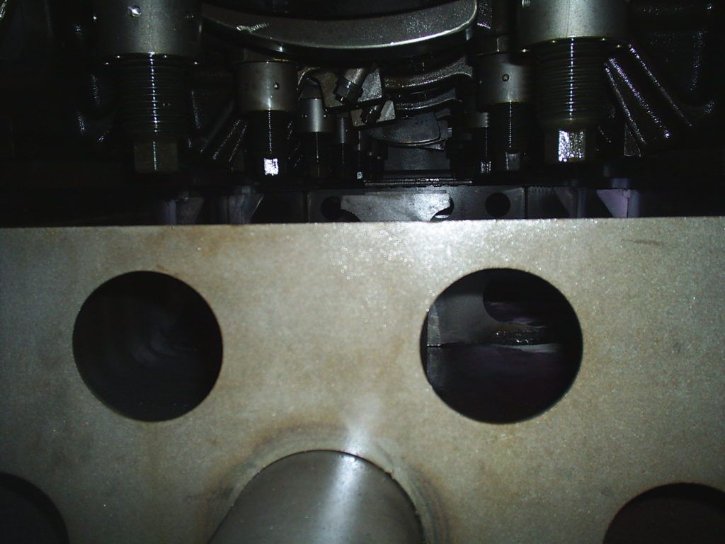 Close-up of a metal panel with two circular holes and a central curved notch under dark machinery.