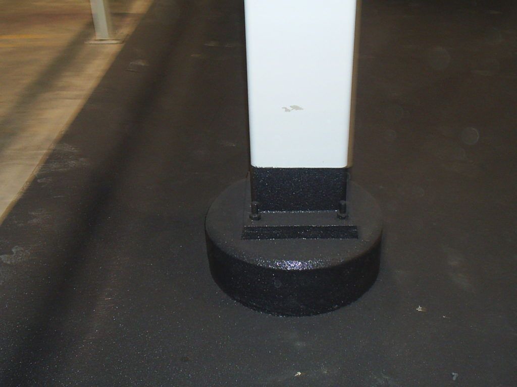 Close-up of a white post on a black base on a dark floor, with a small crack visible near the bottom