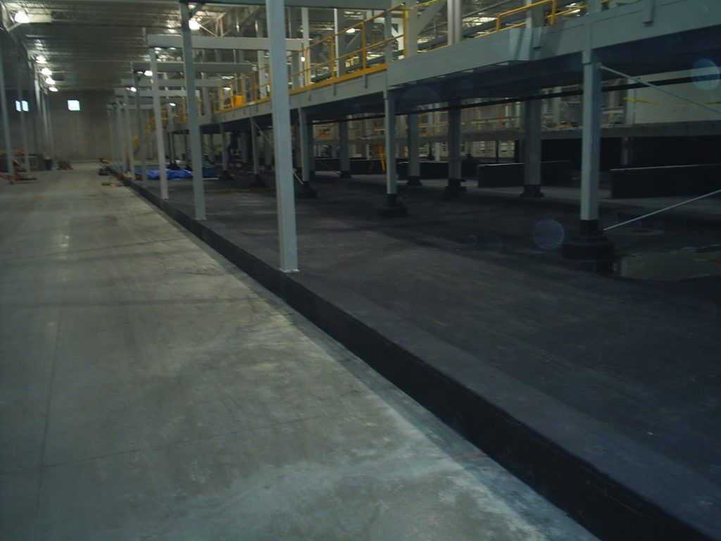 Empty warehouse loading area with concrete floor, metal supports, and parked vehicles in dim light