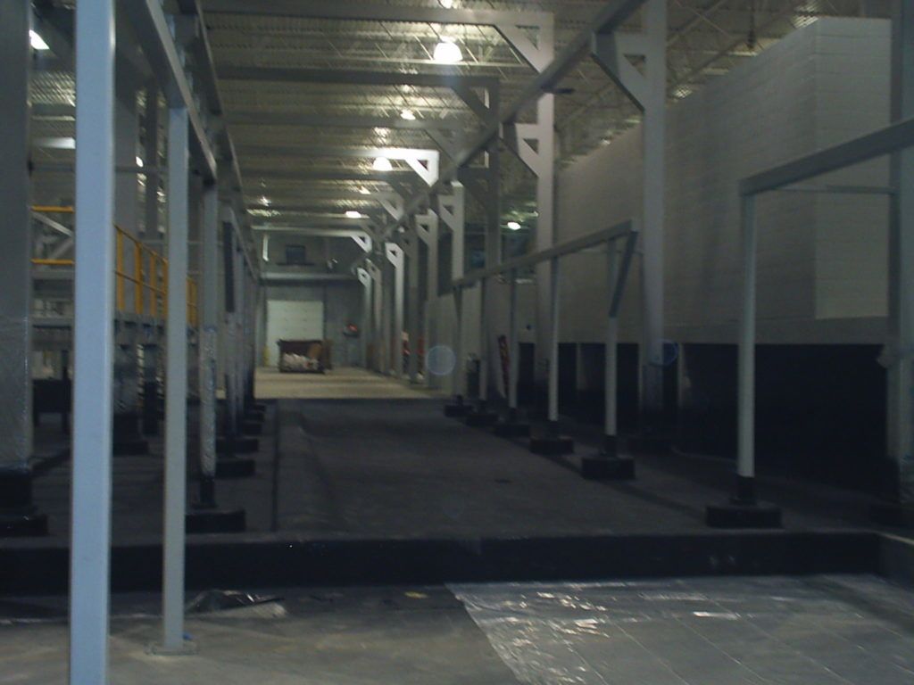 Empty industrial walkway with overhead beams, white columns, and a dark path receding into the distance