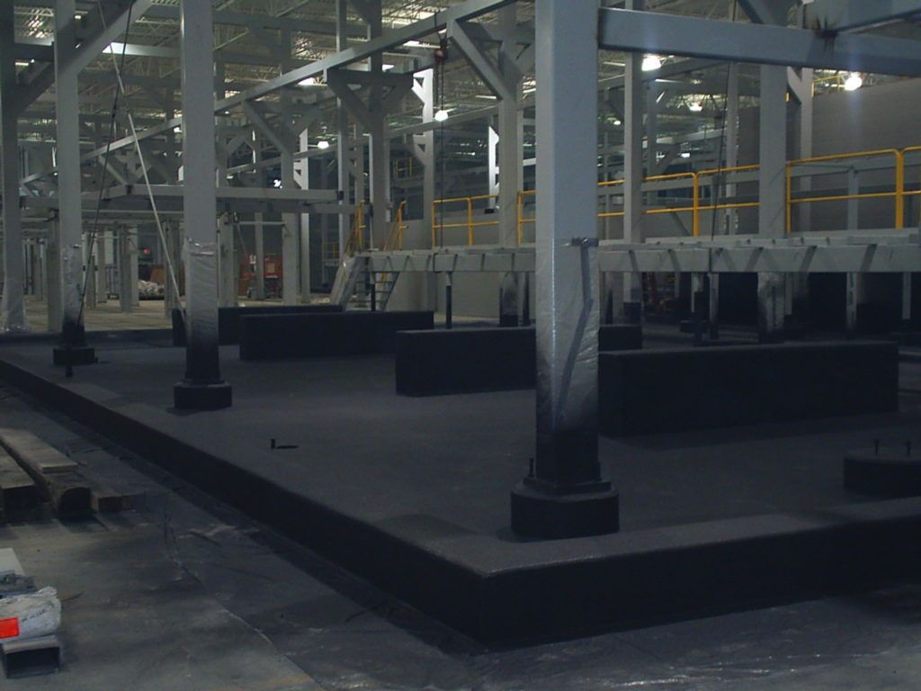 Interior of an empty industrial warehouse with metal beams, platforms, and railings on a concrete floor