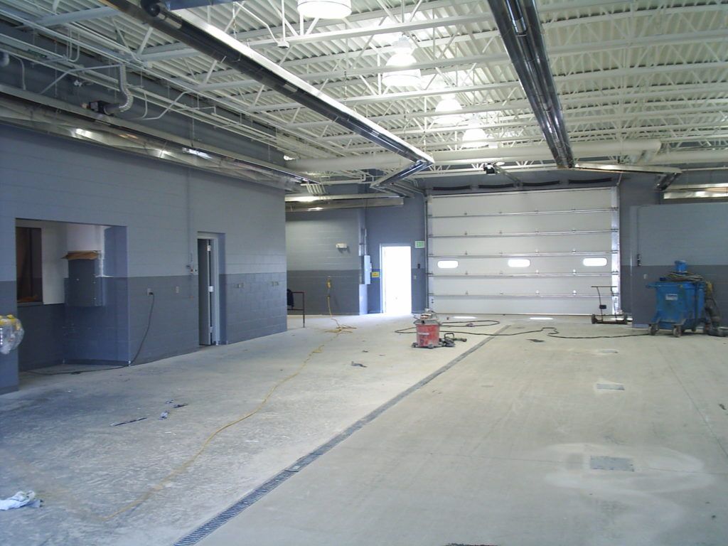 Empty industrial warehouse interior with concrete floor, exposed ceiling, and large garage door.