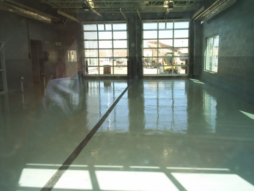Indoor industrial space with a polished wet floor reflecting large windows and overhead lights