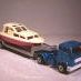 Two toy cars in a snowy scene, a white car being towed by a blue truck