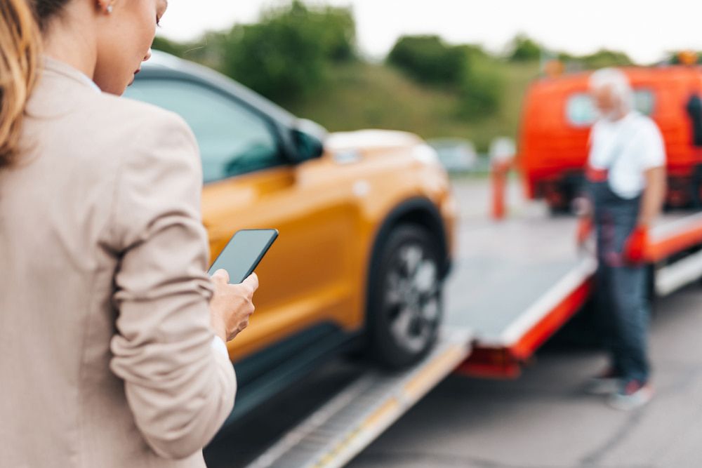 Woman on Phone Watches Her Yellow Car Being Towed — Fulgi's South Coast Automotive and Dismantling in Batemans Bay, NSW