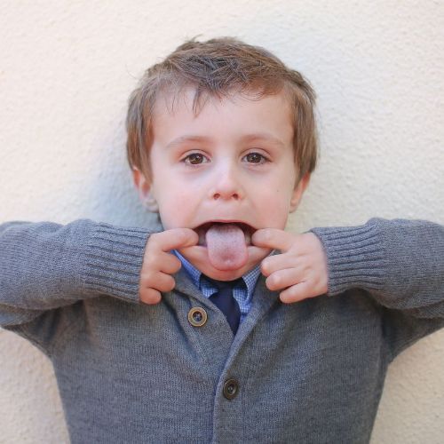 A young boy sticking his tongue out while wearing a grey sweater