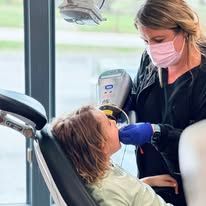 Dentist and child in office; dentist wearing mask, child in chair.