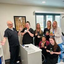 Group of people smiling, holding plants, in a room. One person holds a small jar.