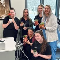 Five women holding potted plants, smiles, in a dental office.
