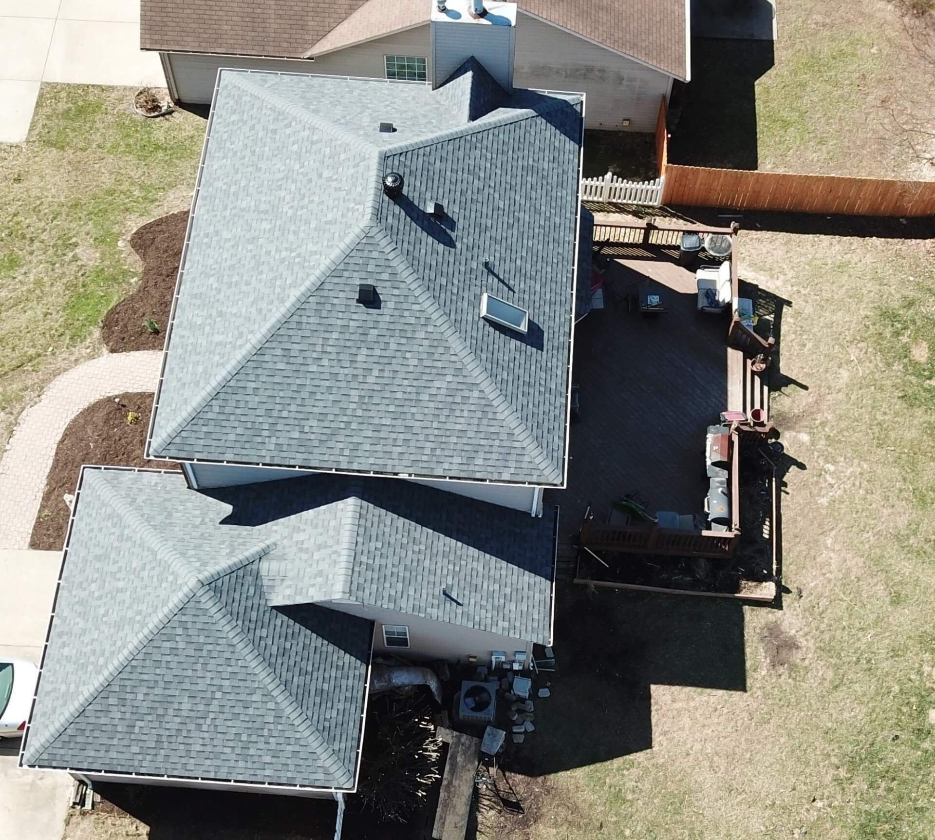 Aerial view of a gray-roofed house with a backyard deck and surrounding lawn.