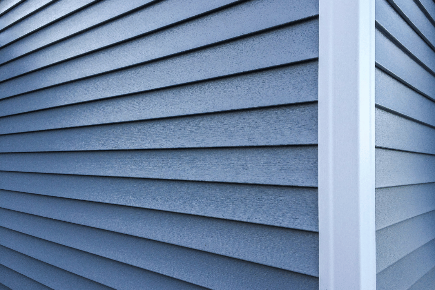 Blue vinyl house siding meeting at a white corner trim detail