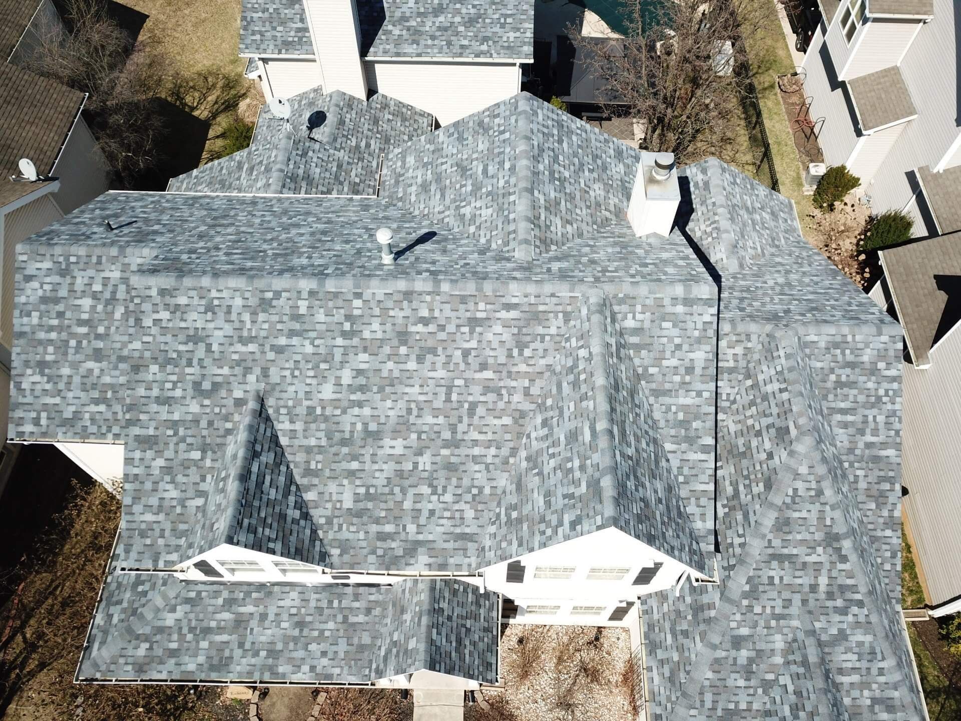 Aerial view of a gray shingled house roof with chimneys and neighboring homes visible.