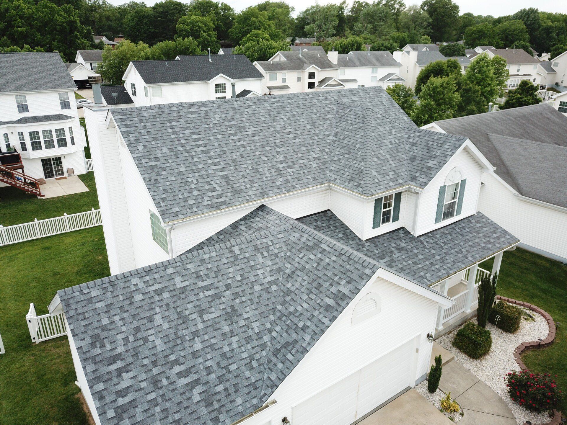 Aerial view of a white suburban house with gray shingle roofs and a curved front walkway.