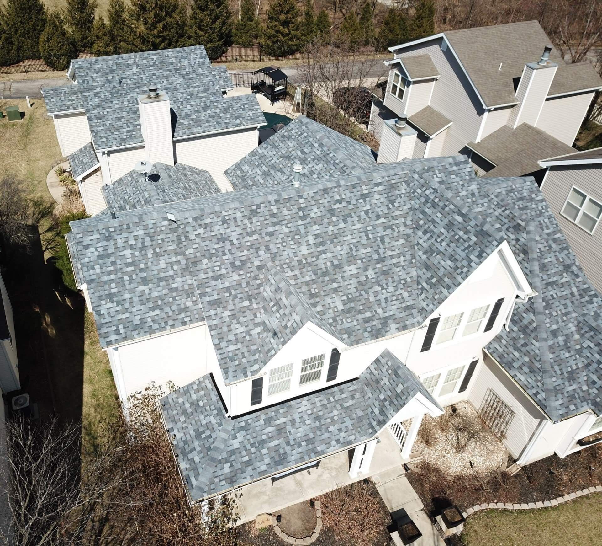 Aerial view of several white houses with gray shingle roofs in a suburban neighborhood.