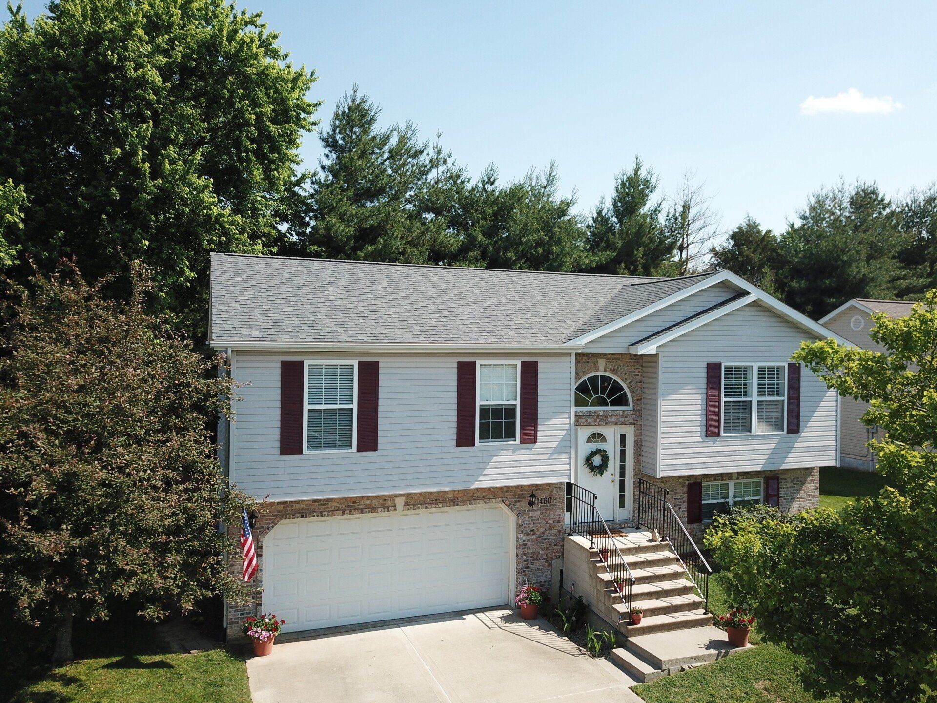 Suburban two-story house with white siding, maroon shutters, garage, and front steps surrounded by trees