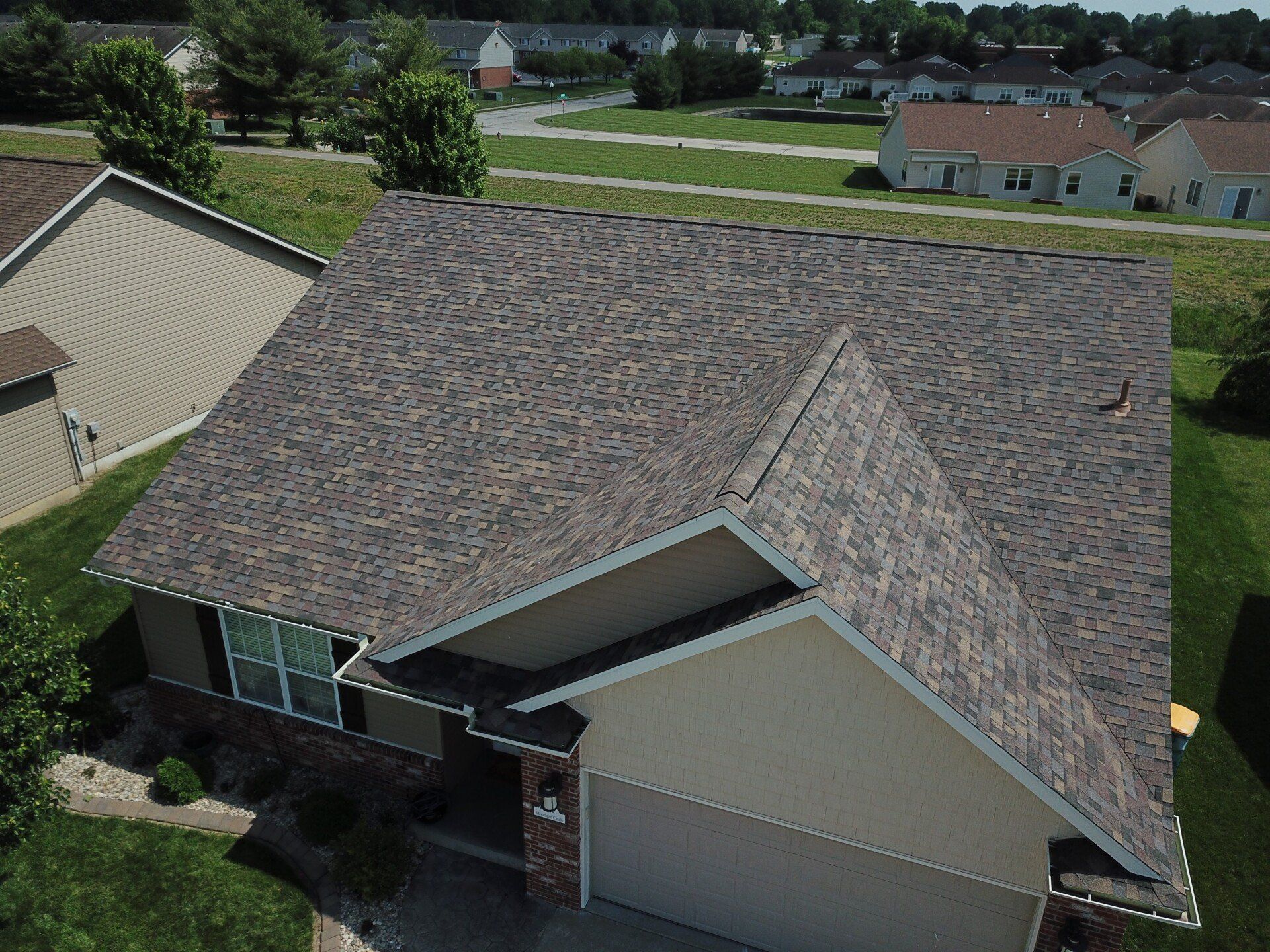 Aerial view of a suburban house with a large shingled roof and driveway, surrounded by neighboring homes and lawns