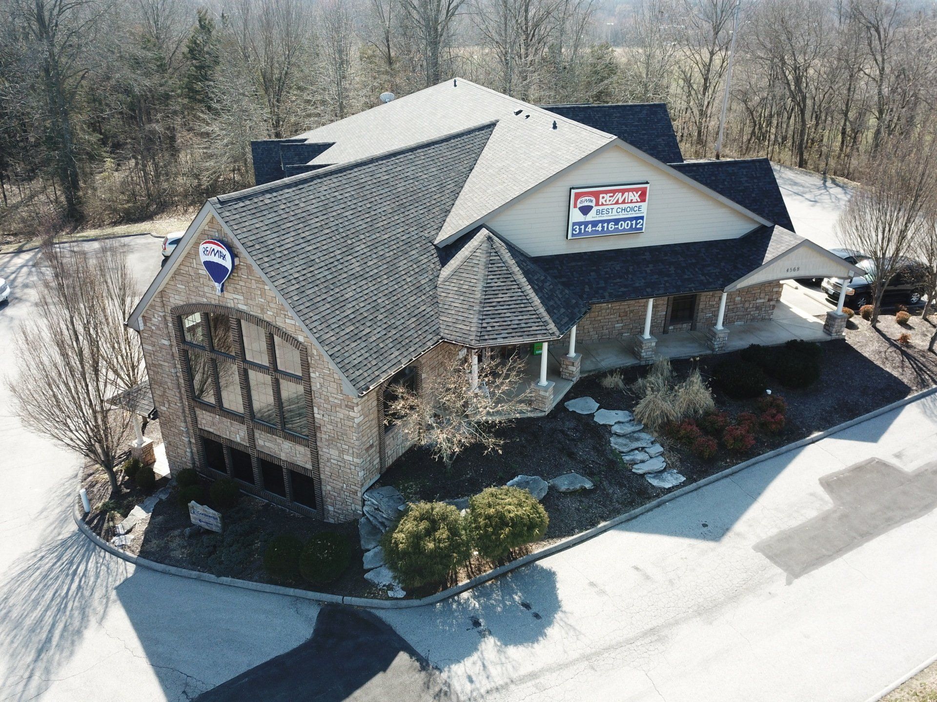 Aerial view of a gray-roofed commercial building with a red-and-blue sign and surrounding parking lot.