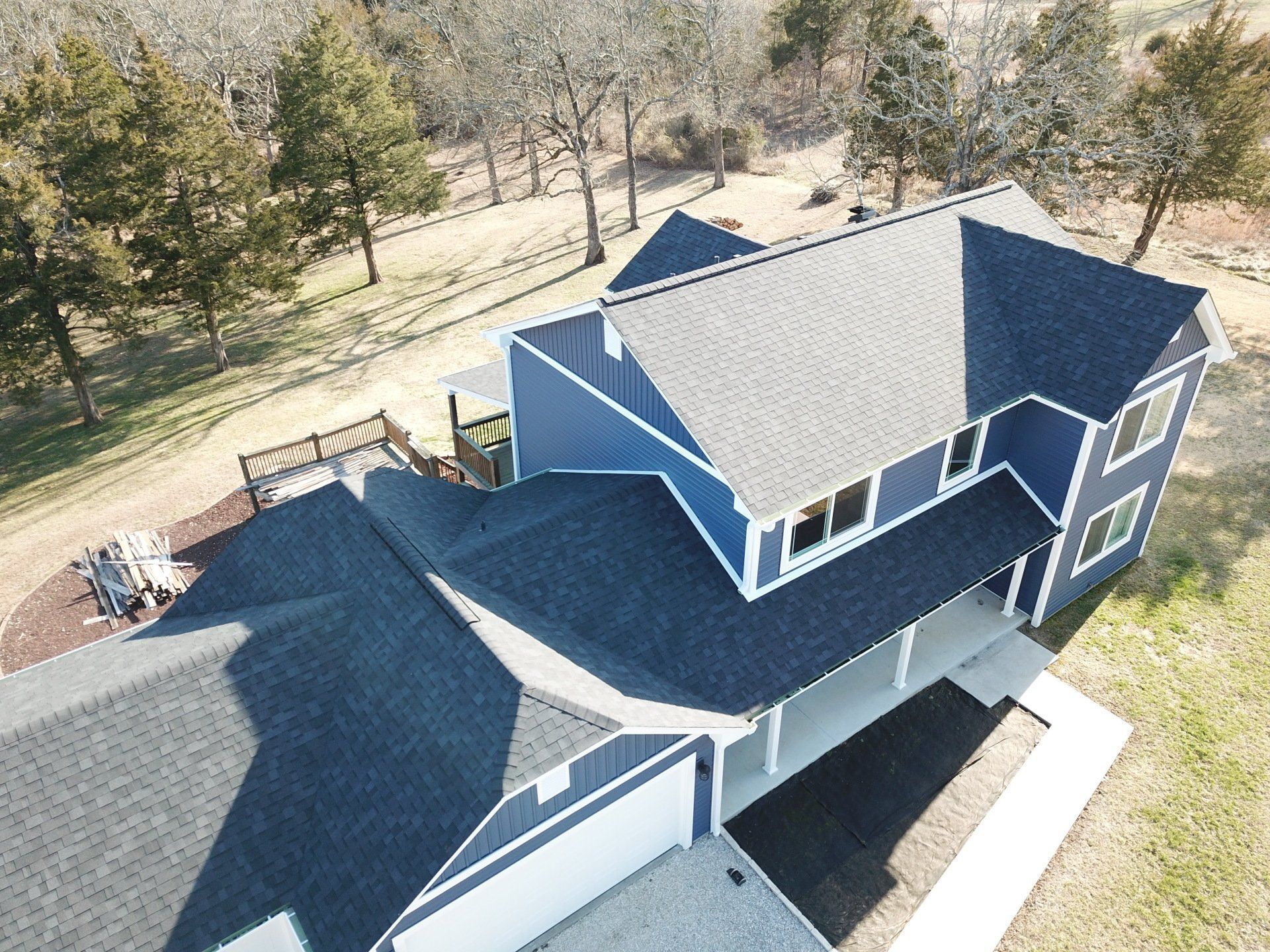 Aerial view of a blue-gray house with a large driveway and surrounding trees.