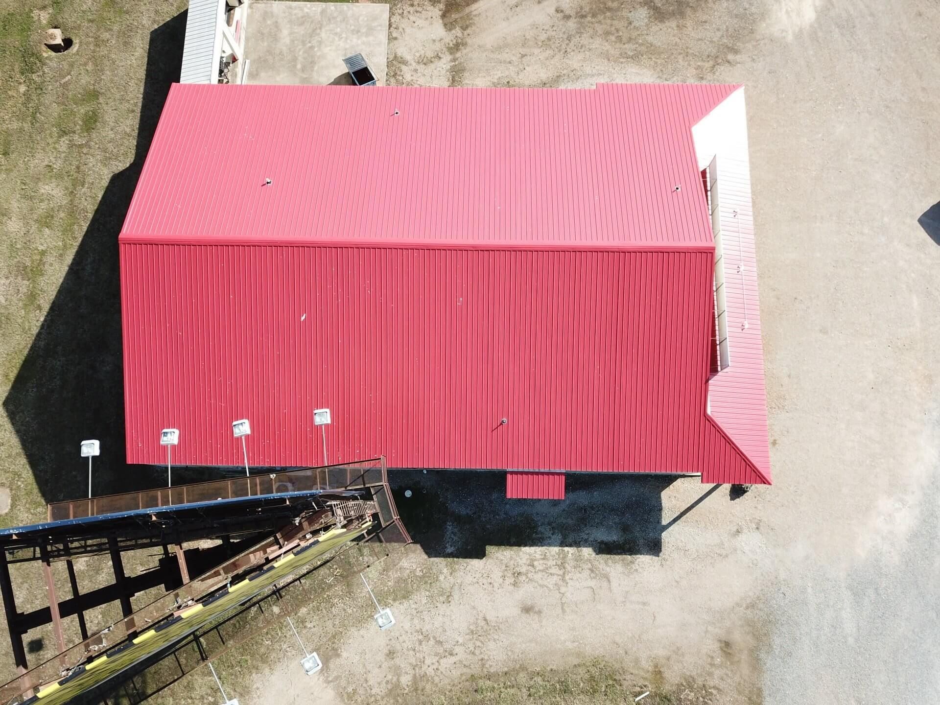 Aerial view of a red-roofed building beside a driveway and wooden stairway.