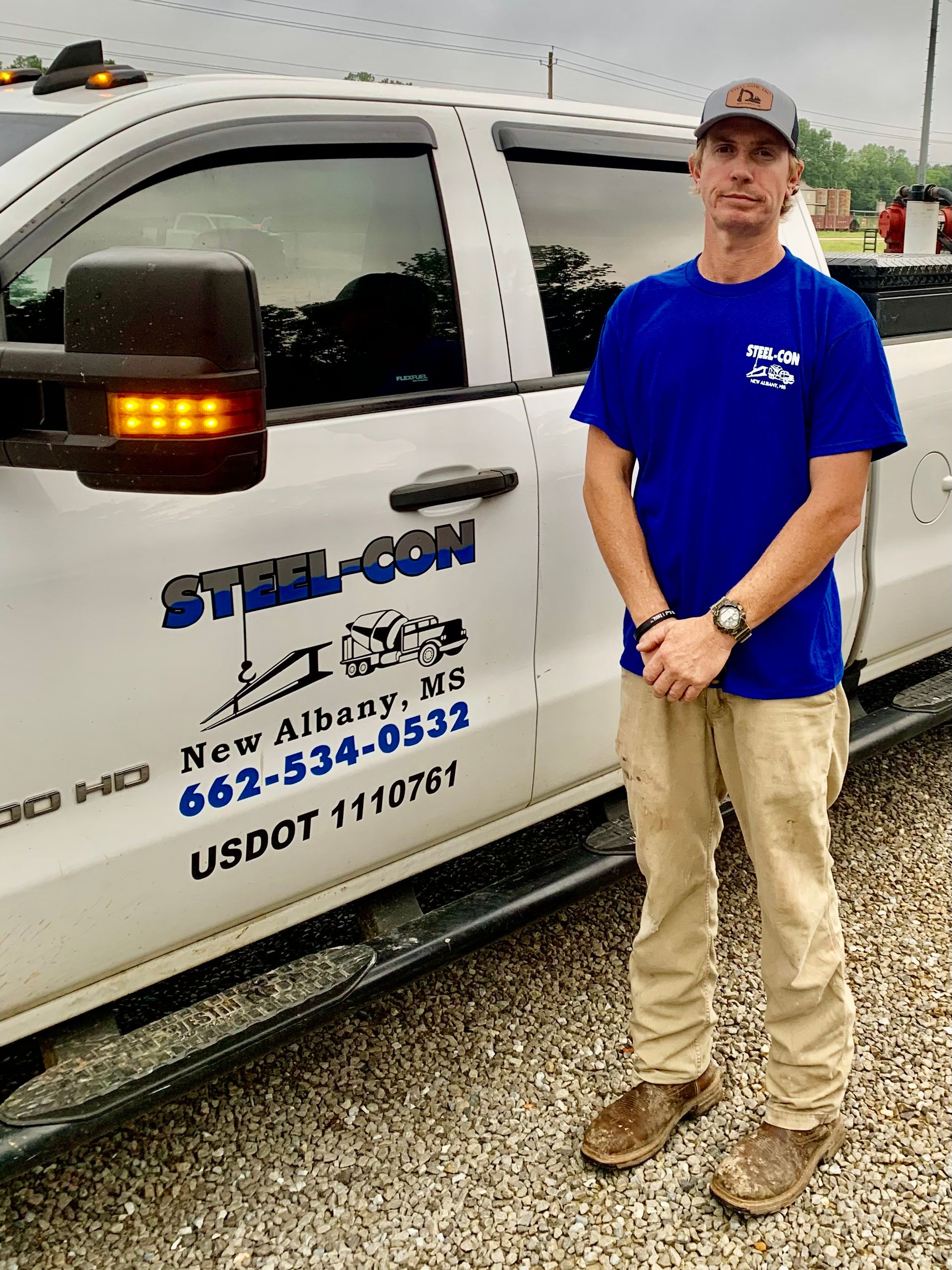 A man in a blue shirt is standing in front of a white truck.