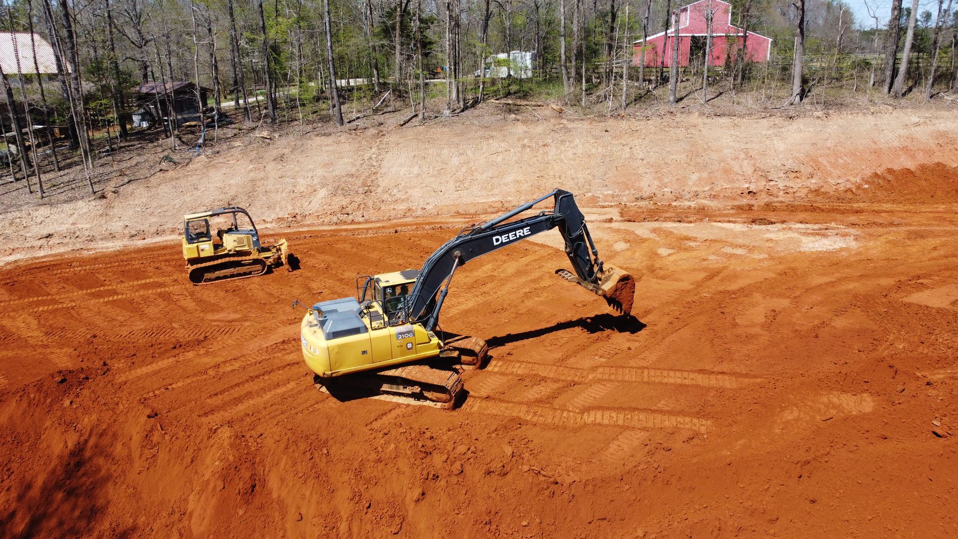 A yellow excavator is moving dirt in a field next to a bulldozer.