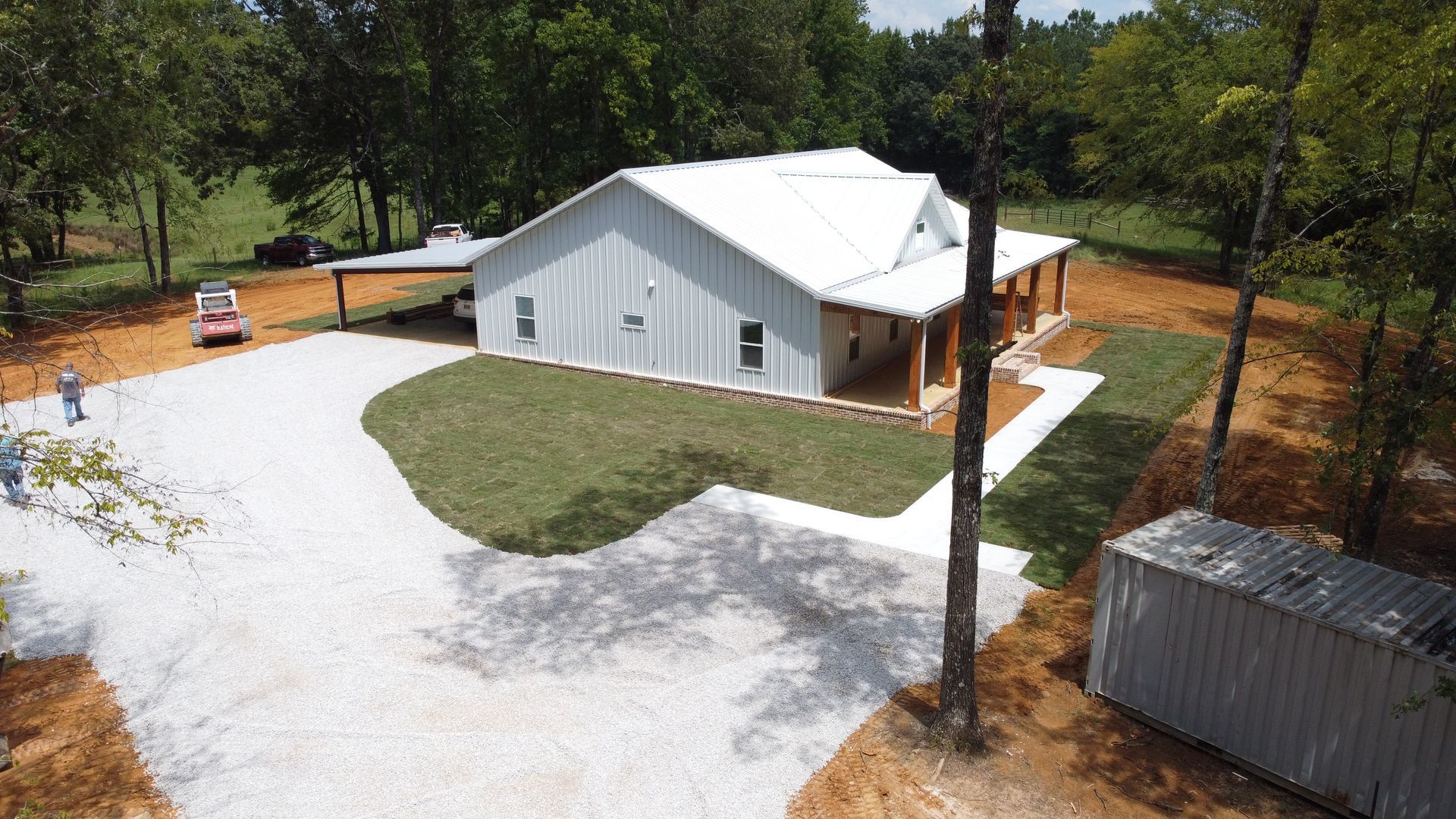 An aerial view of a large white house with a driveway and a porch surrounded by trees.