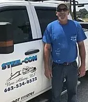 A man in a blue shirt is standing next to a white truck.