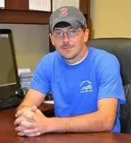 A man is sitting at a desk wearing a baseball cap and glasses.