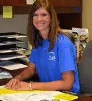 A woman in a blue shirt is sitting at a desk in an office.