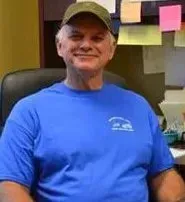 A man in a blue shirt and hat is sitting in a chair.