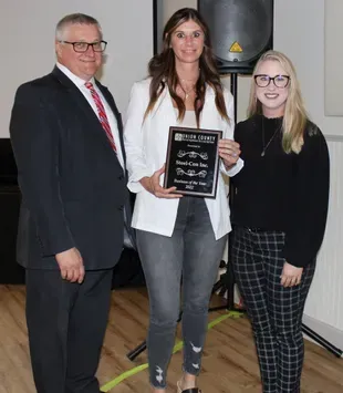 A man in a suit and tie is standing next to two women holding a certificate.