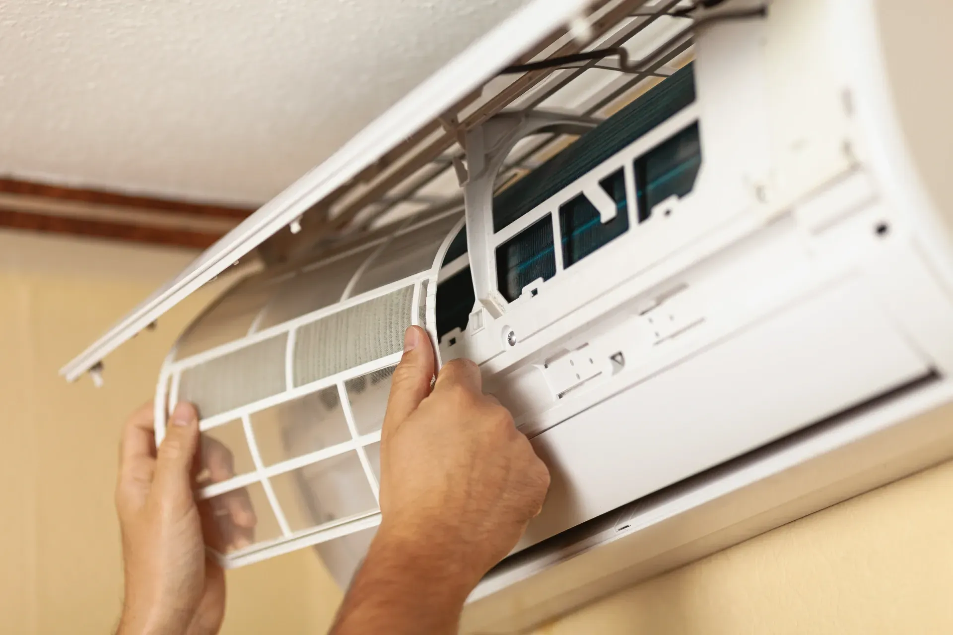 Hands Cleaning the Filter of a Wall-mounted Air Conditioner Indoors — Bes-Elect Electrical in Taminda, NSW