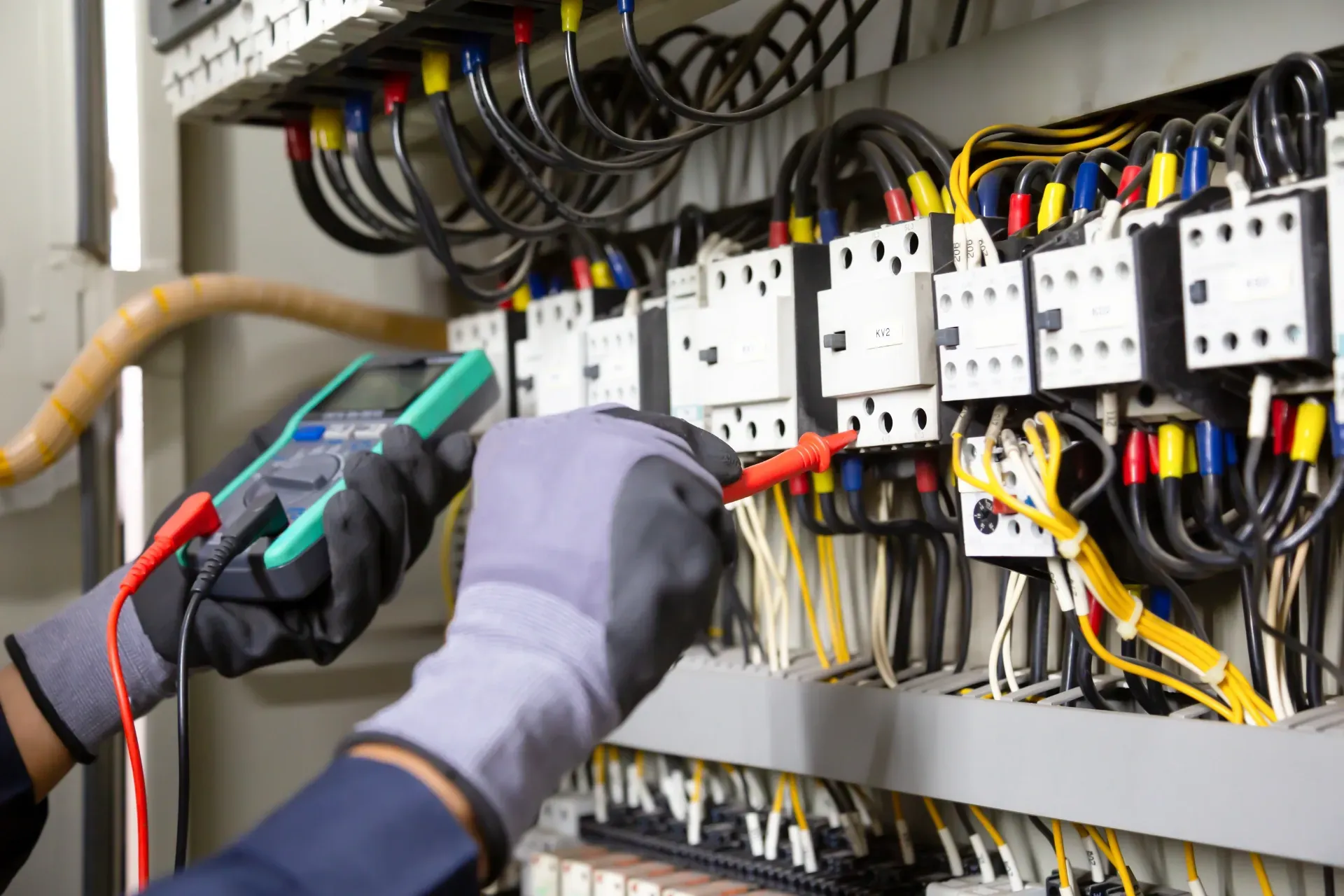 Technician testing electrical control panel wiring with a multimeter and gloved hands — Bes-Elect Electrical in Taminda, NSW