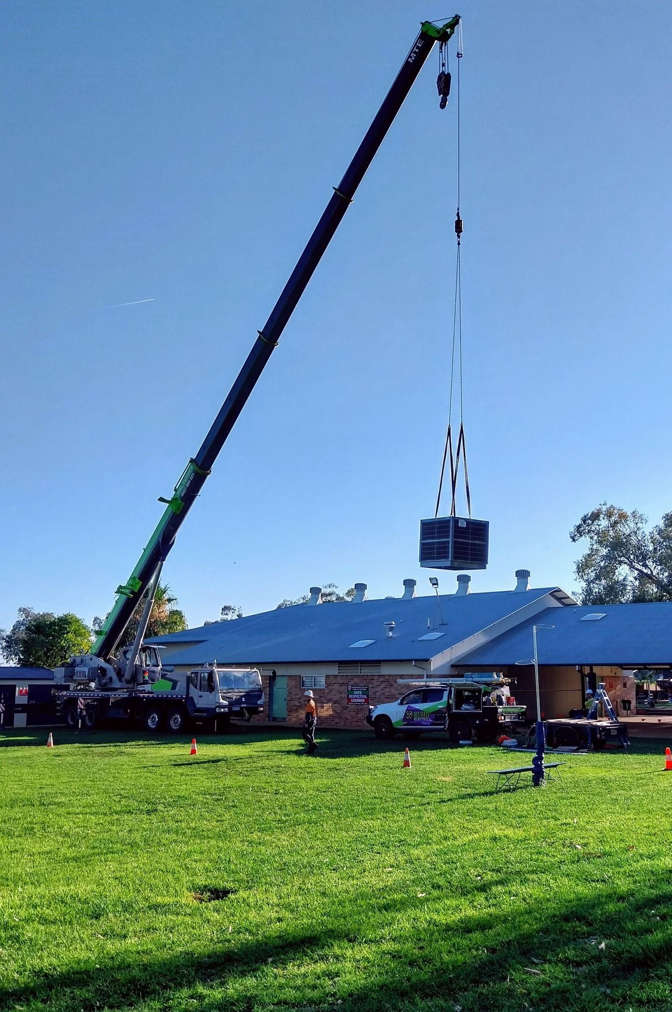 Crane Lifting a Large Black Object Over a Grassy Field Beside a Stadium — Bes-Elect Electrical in Taminda, NSW