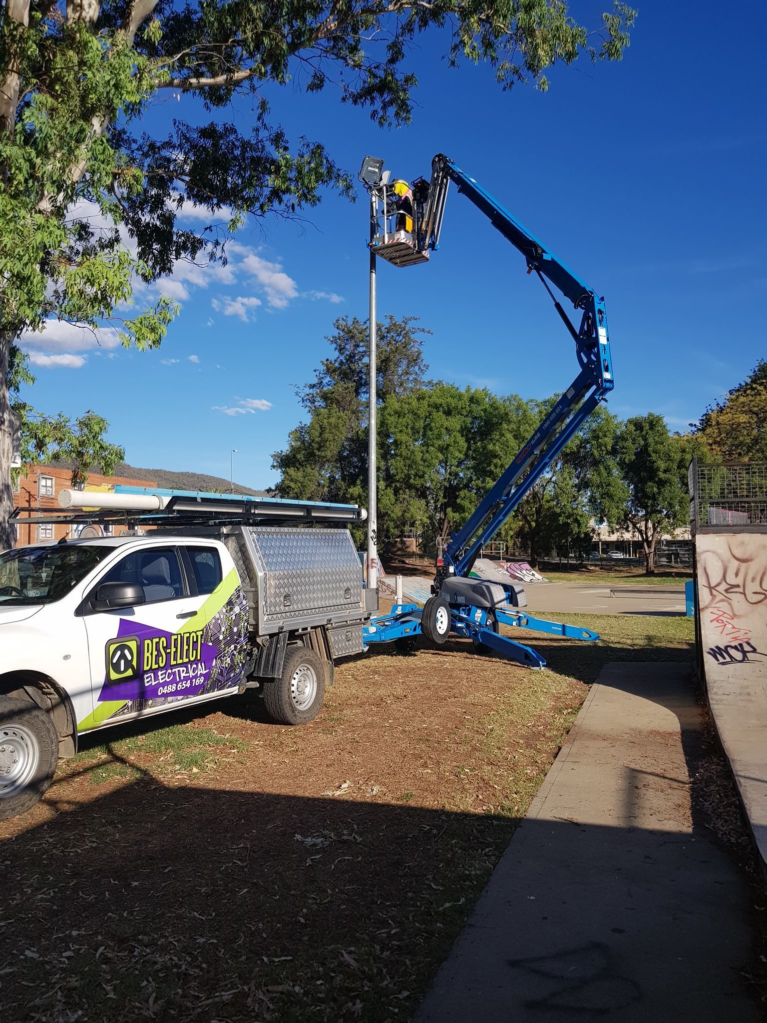 Utility Truck with Bucket Lift Working Beside a Sidewalk Under a Blue Sky — Bes-Elect Electrical in Taminda, NSW