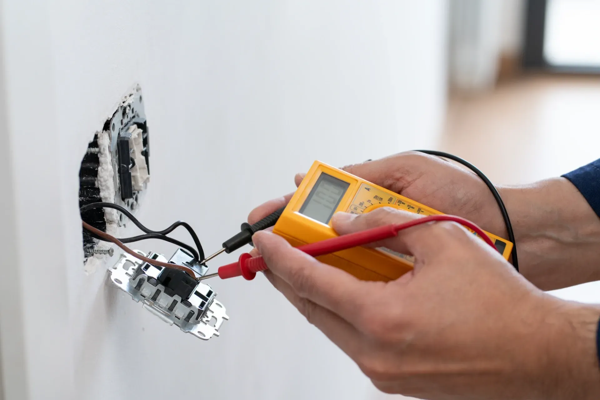 Hand holding a multimeter testing exposed electrical wiring in a wall outlet box — Bes-Elect Electrical in Taminda, NSW