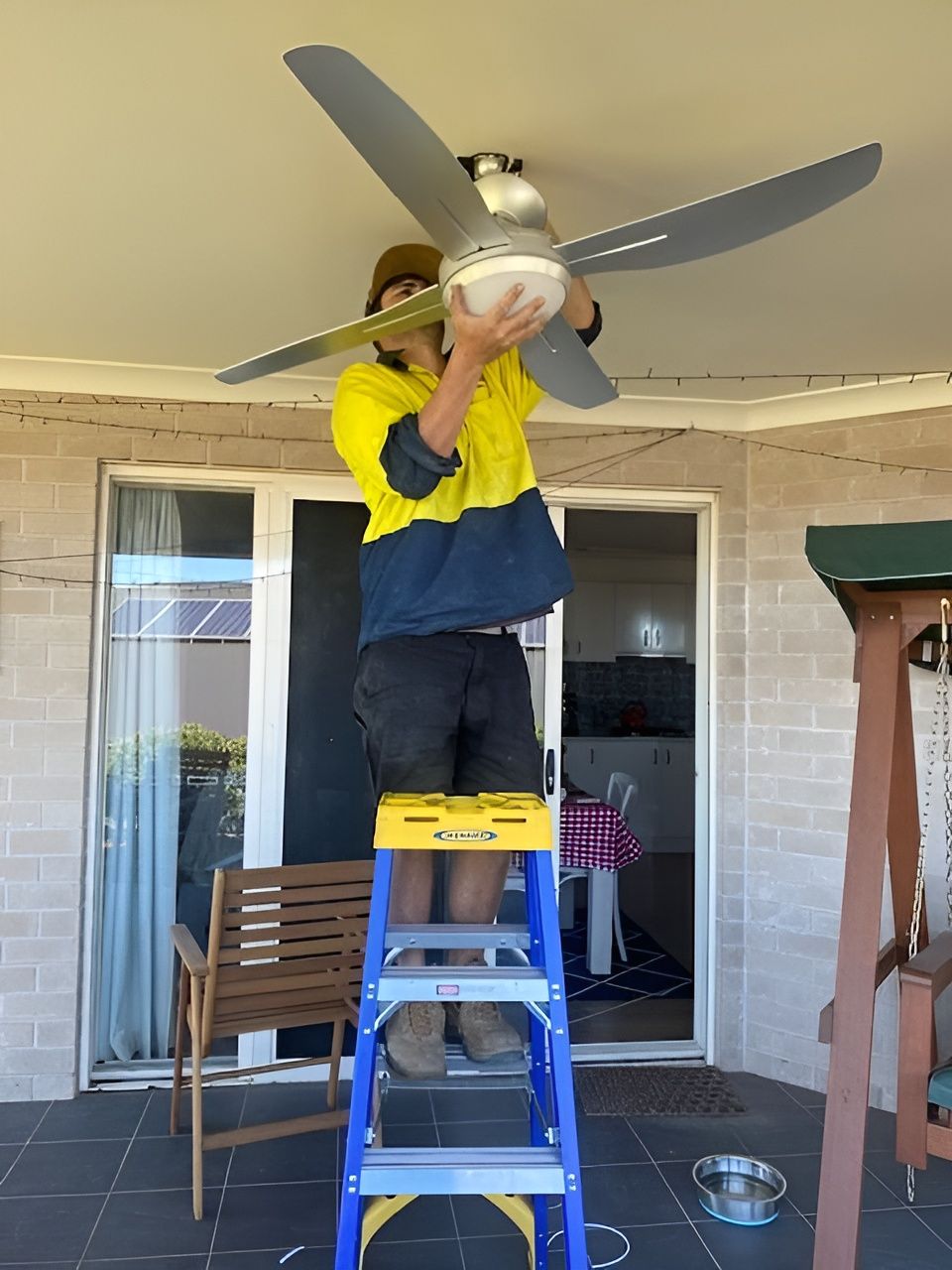 Person on A Blue Ladder Installing a Ceiling Fan on A Porch — Bes-Elect Electrical in Taminda, NSW